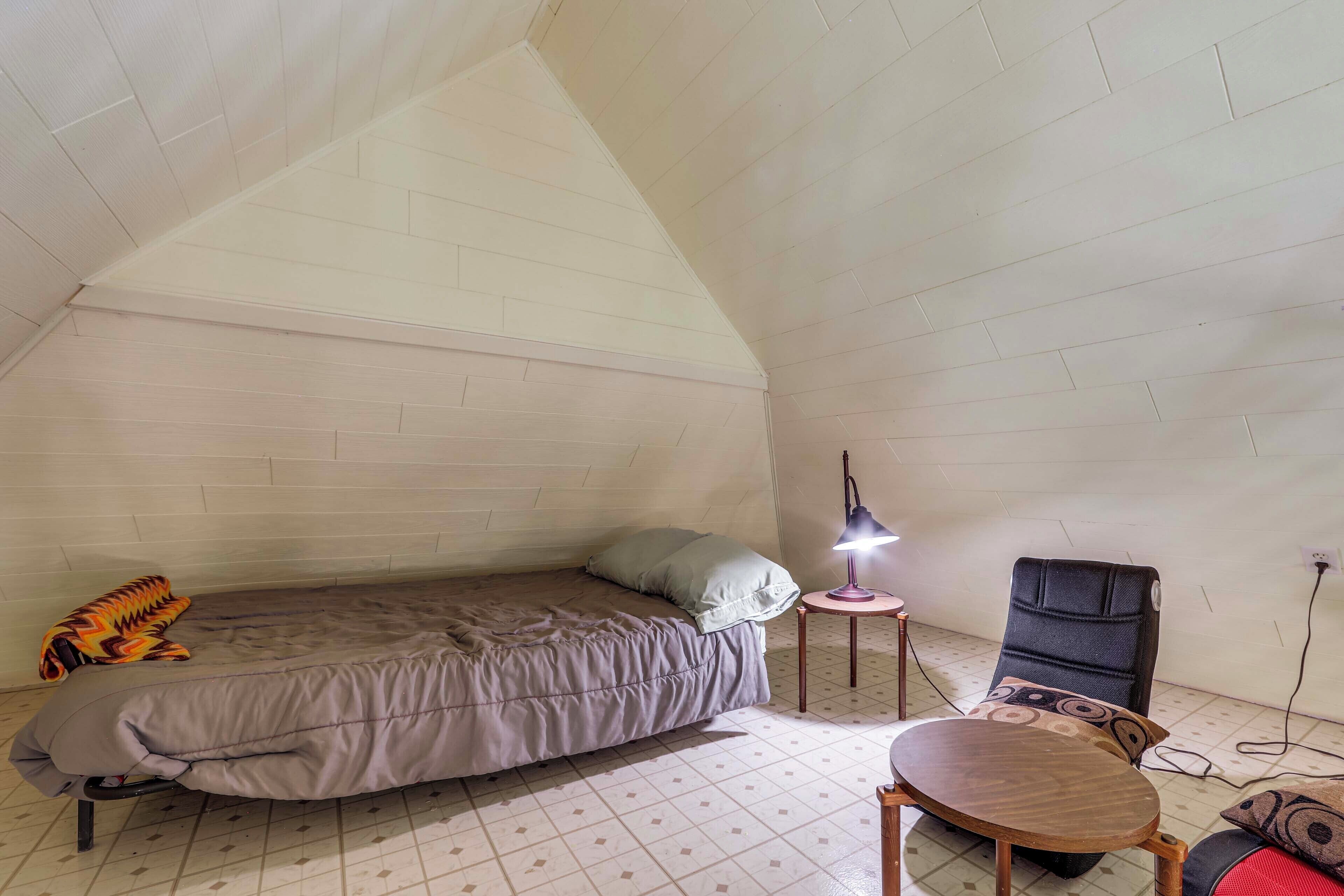 Ein kleiner, dreieckiger Dachraum mit einem Bett, einem Tisch und einem Stuhl.
