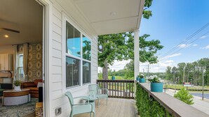 A porch with a wooden deck, a seating area with chairs and a table, and a view of the street and trees.