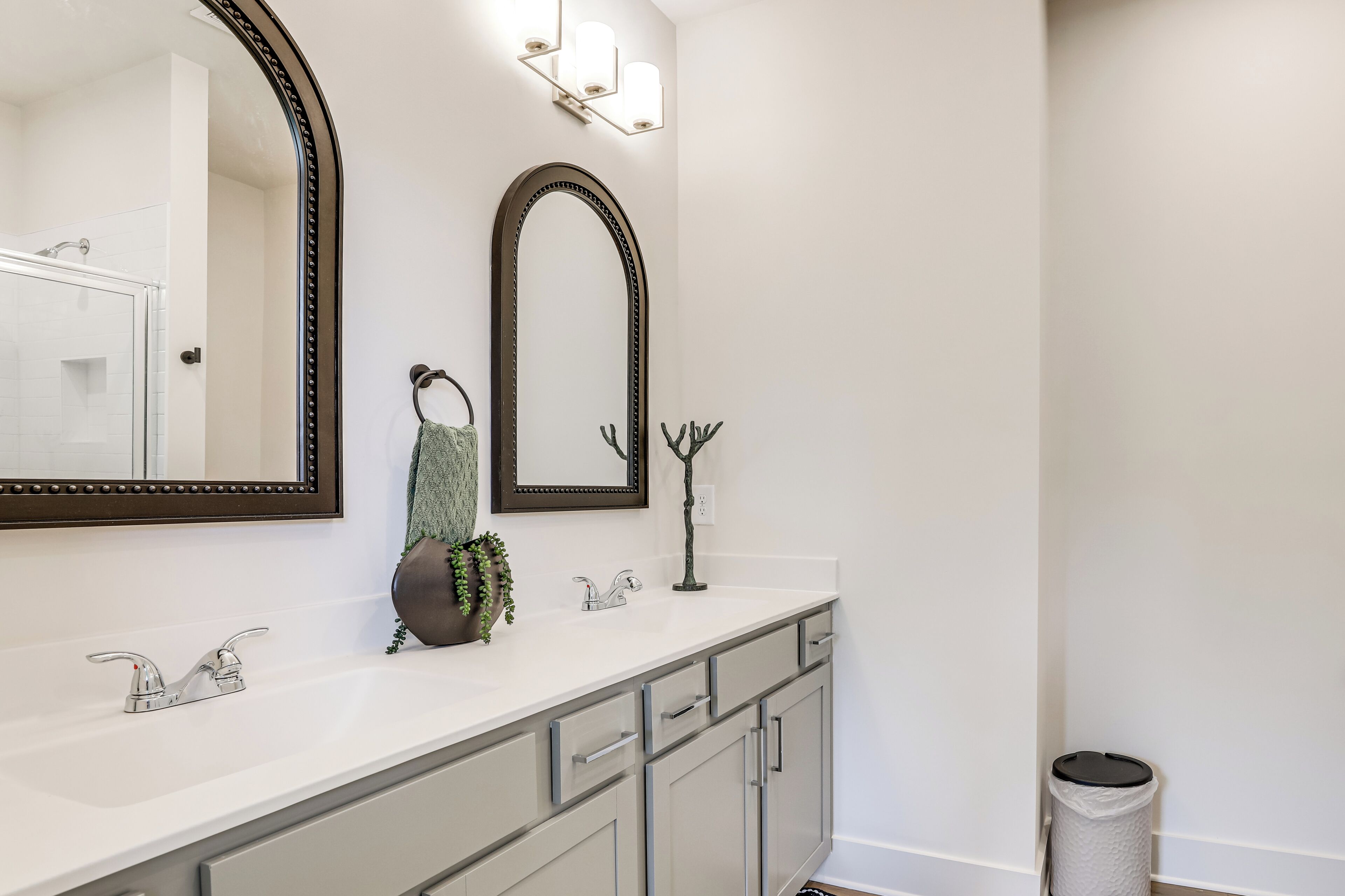 A bathroom with a large mirror, two sinks, a towel rack, and a trash can.