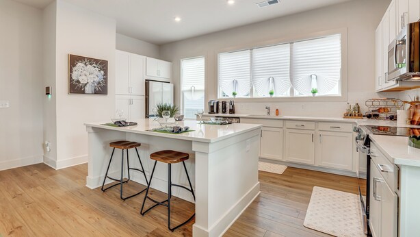 A modern kitchen with white cabinets, a large island with stools, and a window with blinds.