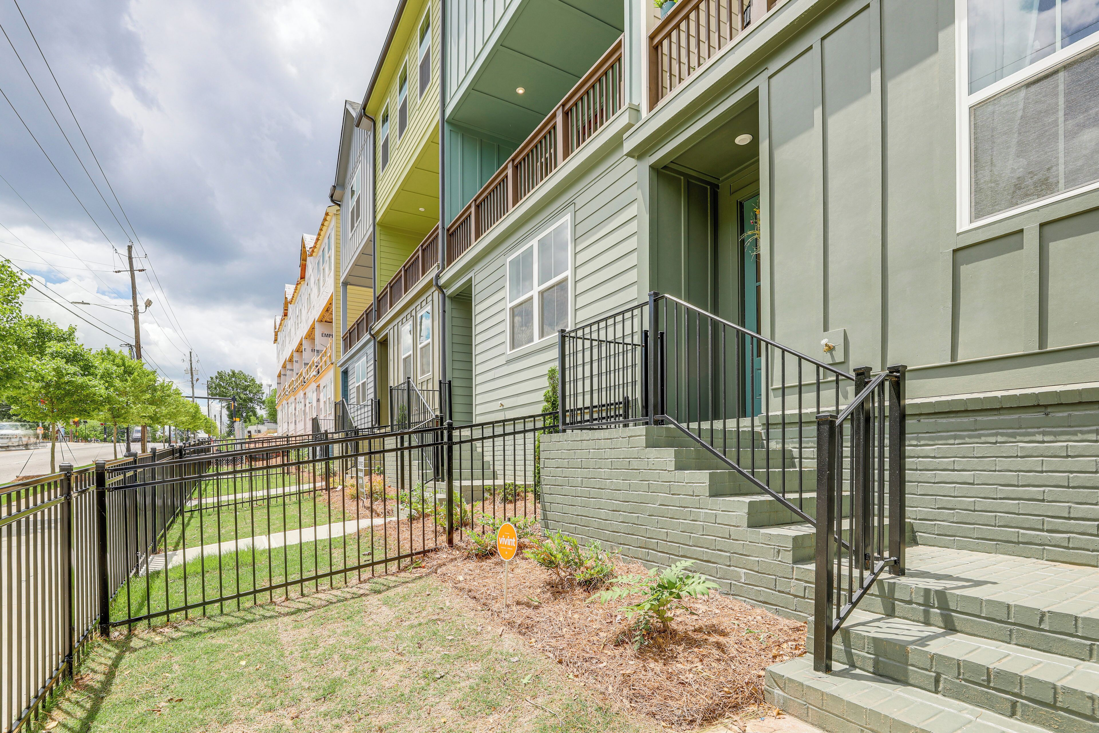 A multi-story residential building with a green exterior, a black metal fence, and a small garden area.