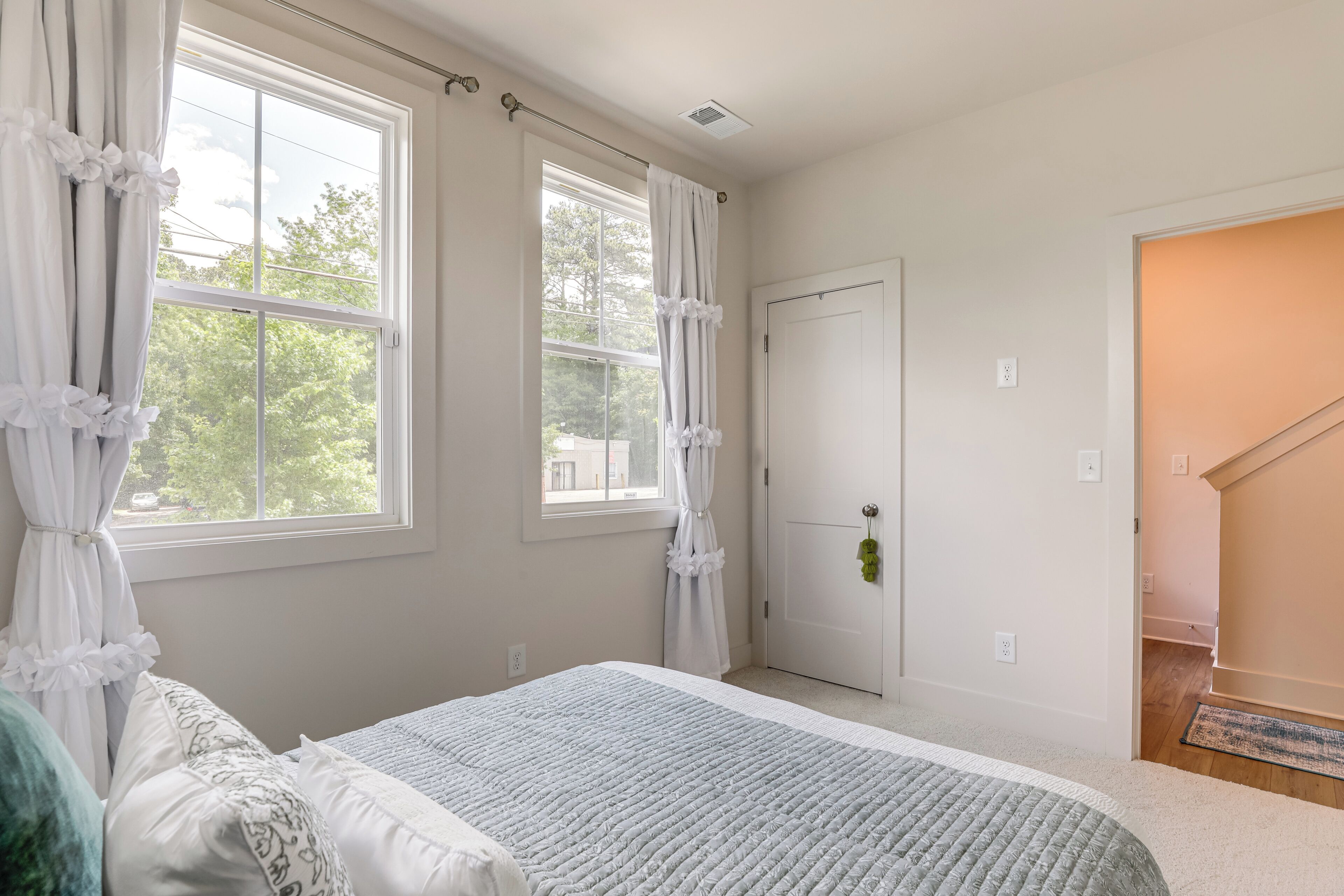 A bedroom with a bed, two windows with curtains, a door, and a staircase.