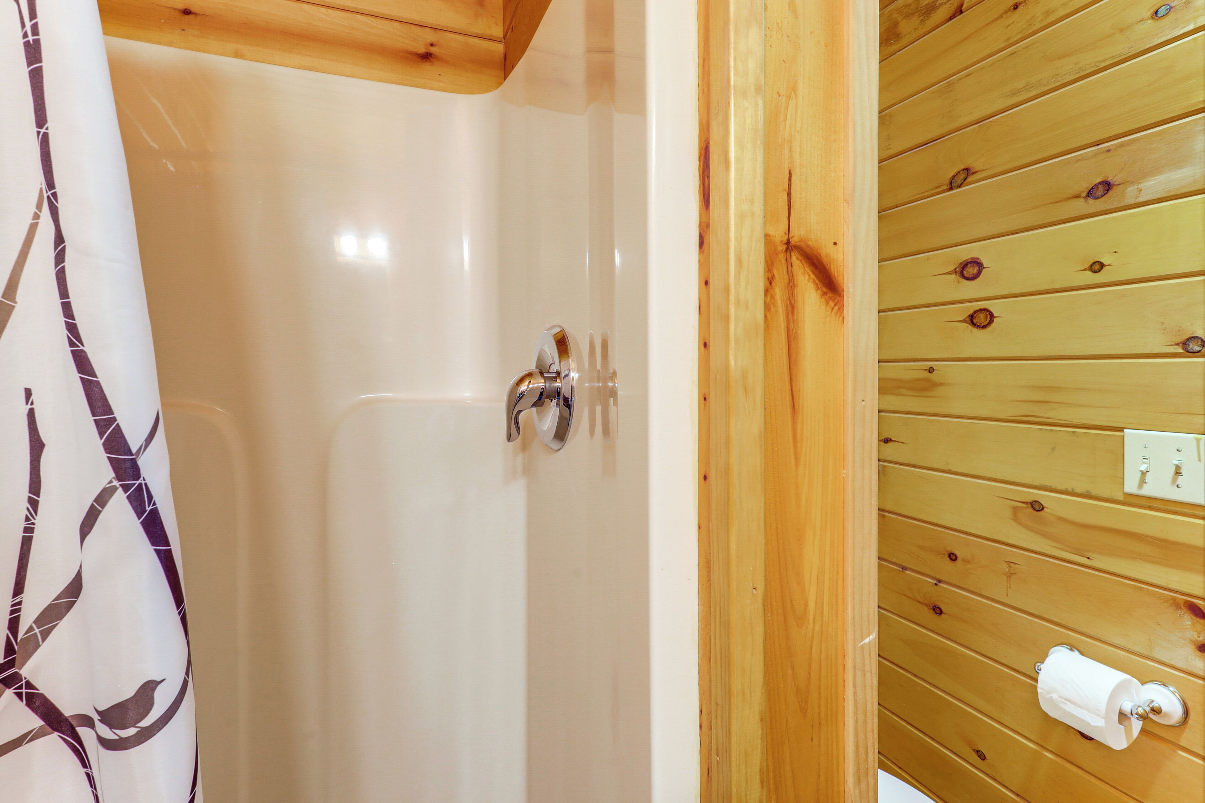 Une salle de bain avec un mur en bois, un rideau de douche et un porte-rouleau de papier toilette.