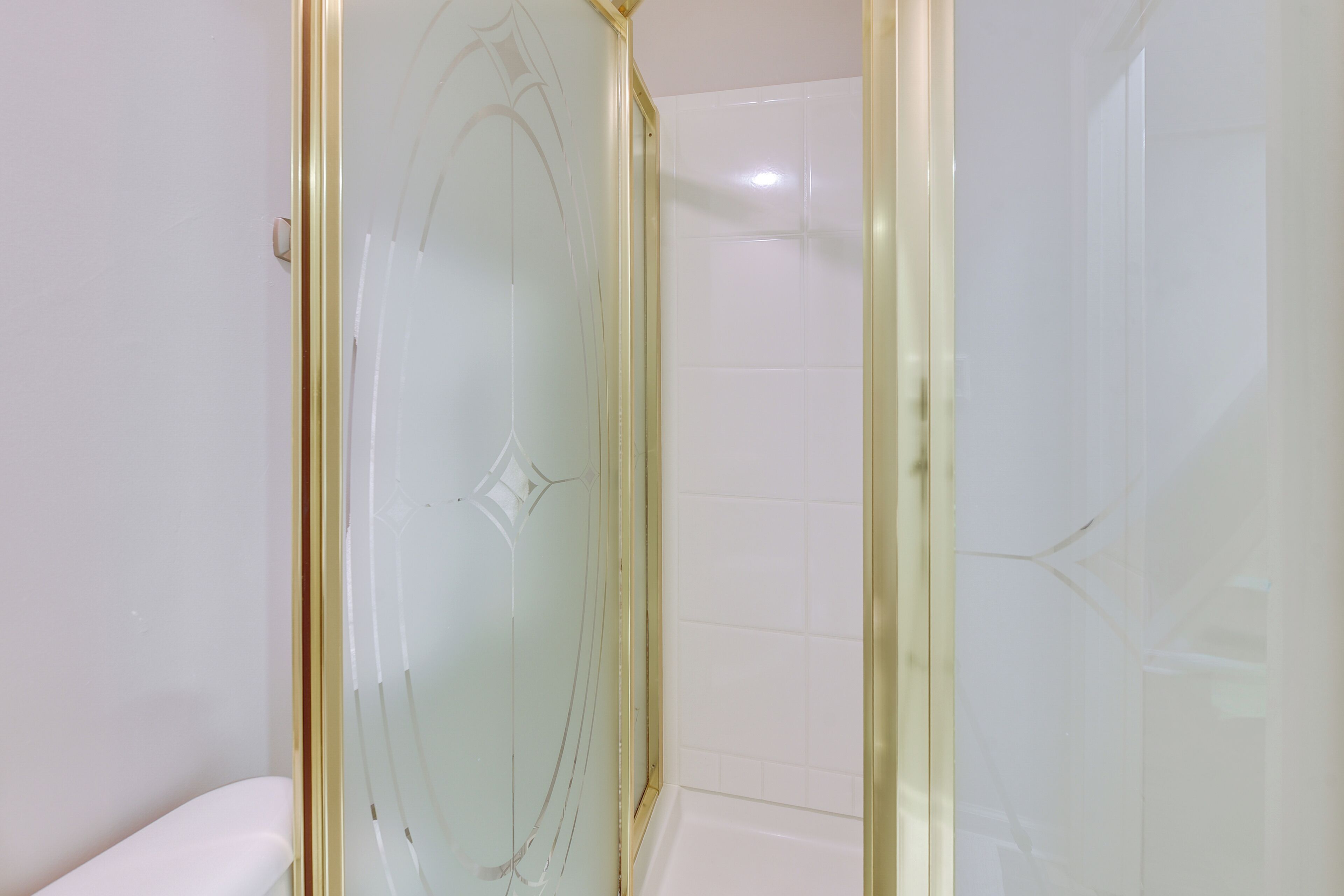 Een badkamer met een douchecabine van glas, witte tegels en een wit toilet.