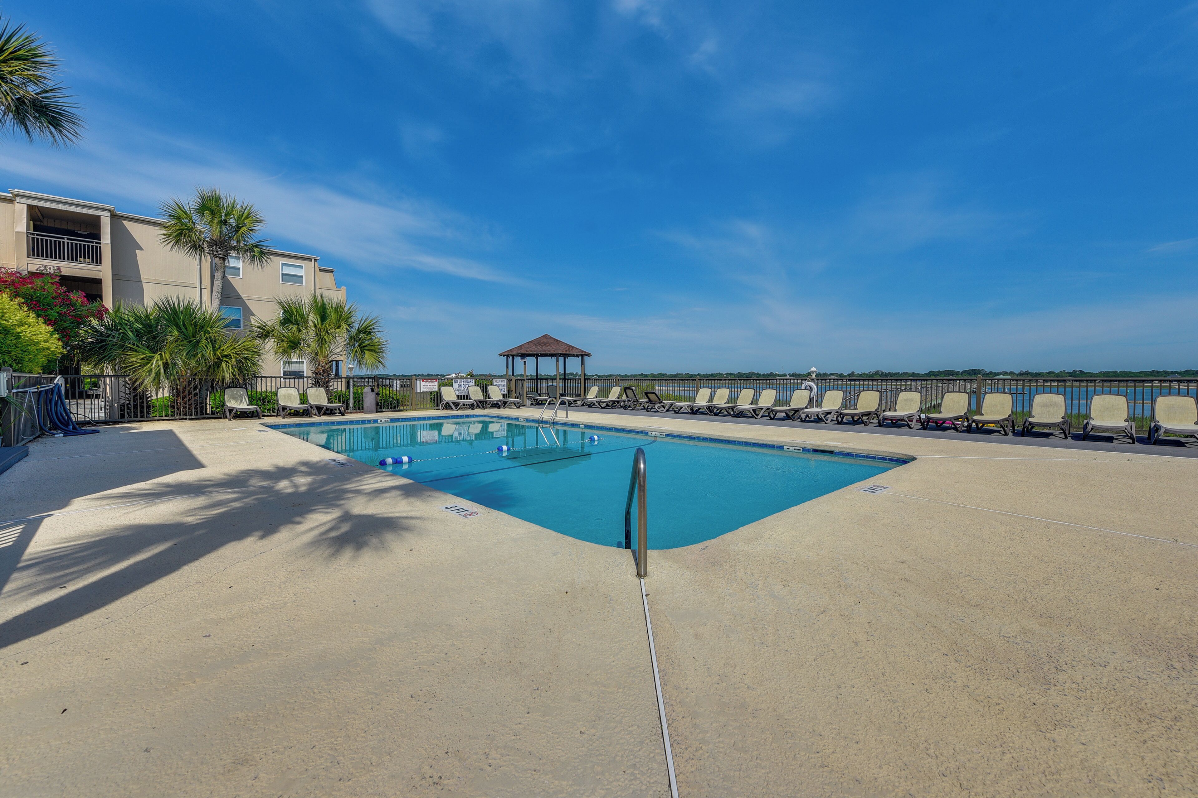 Une piscine avec des chaises longues, un kiosque et un bâtiment doté de balcons.