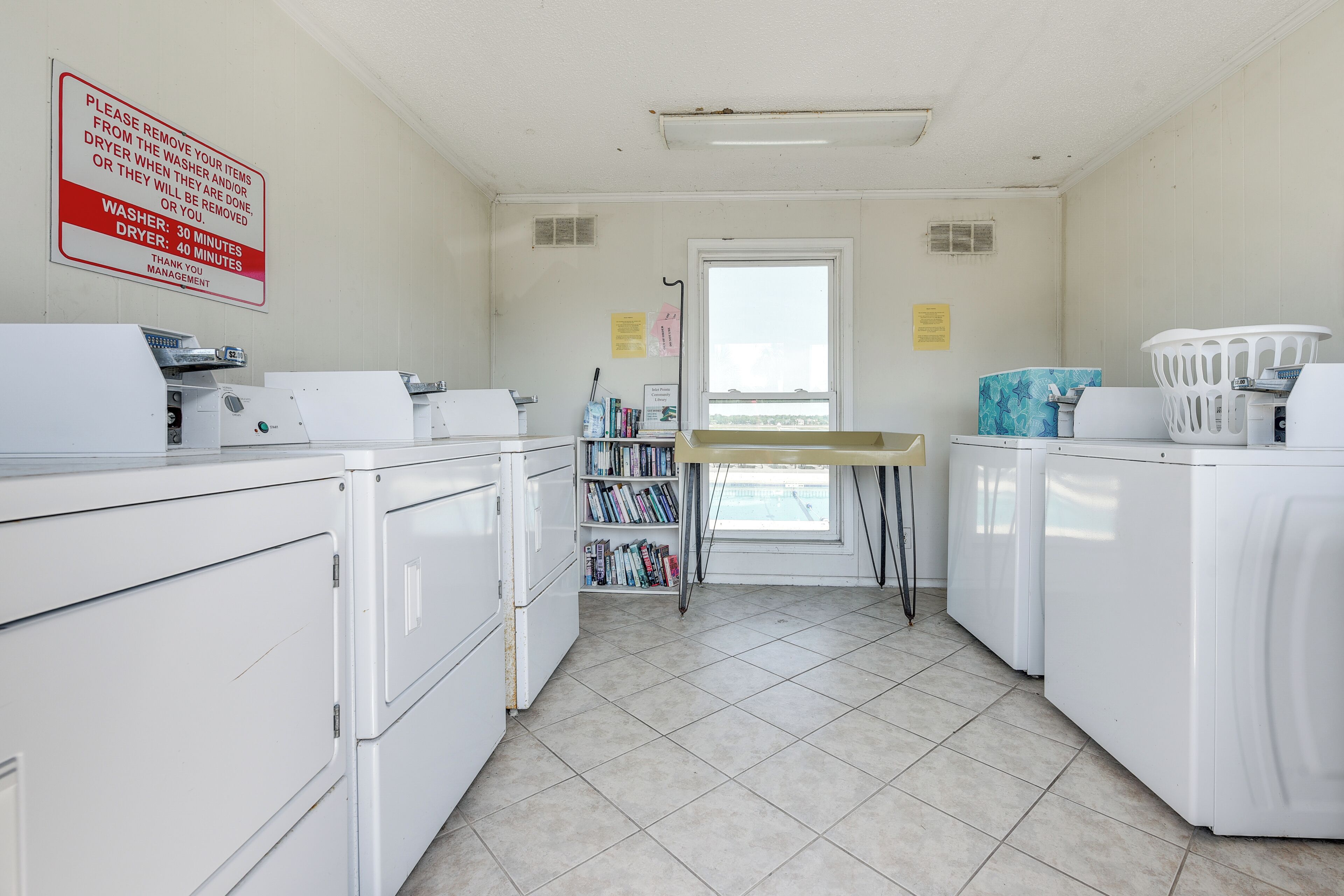 A laundry room with white washers and dryers, a drying rack, and a window with a view.