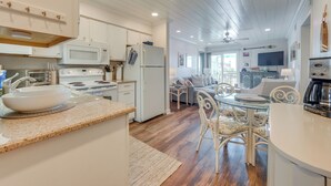A modern kitchen with white cabinets, a microwave, and a refrigerator. There is a dining area with a glass table and white chairs. - Walk to Beach & Marsh: Condo in Murrells Inlet (Murrells Inlet)