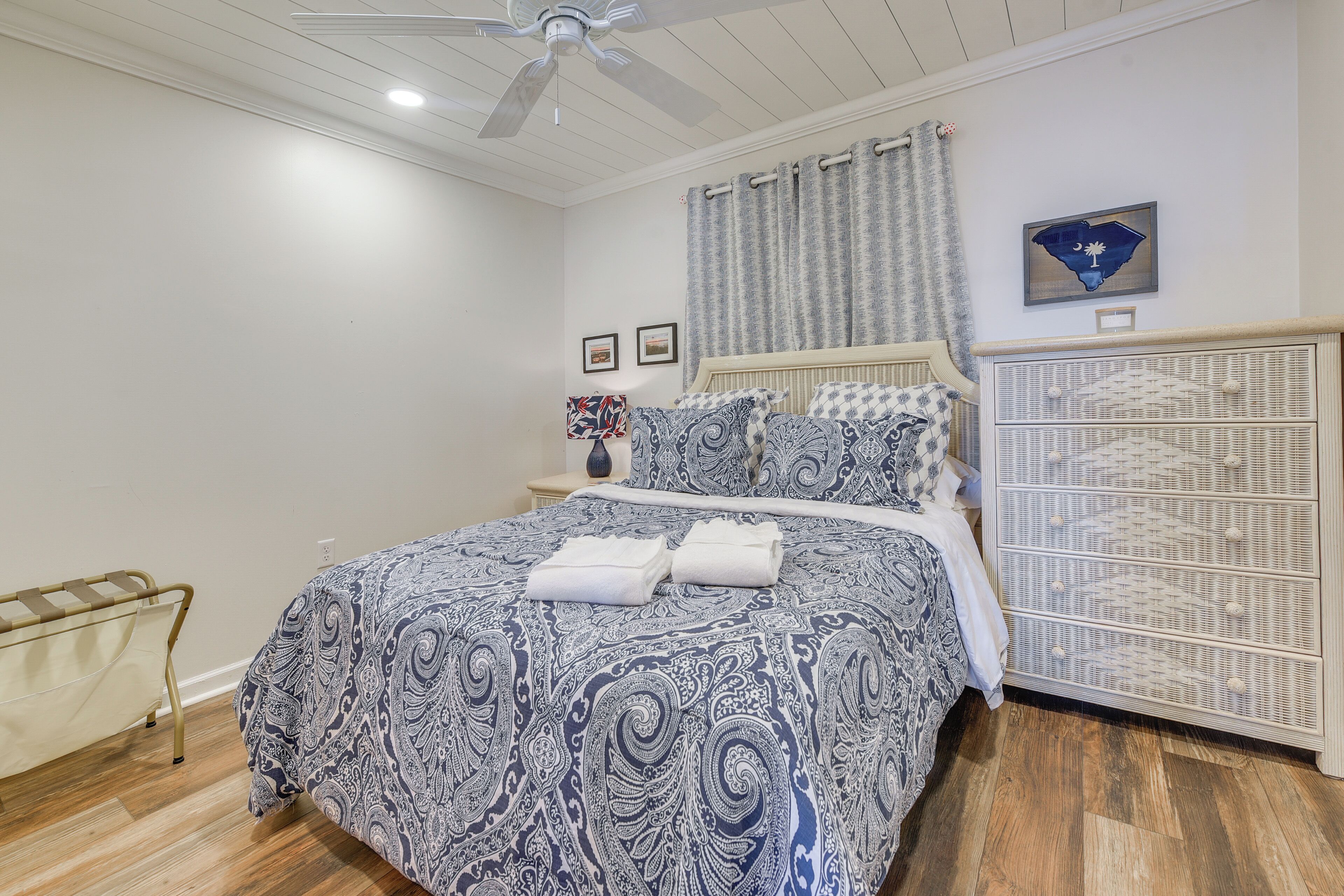 Un dormitorio con cama, ventilador de techo, mesita de noche y cómoda.