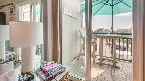 A balcony with a view of a residential area, a sign reading "MURRILL'S INLET," and a table with magazines and a lamp. - Walk to Beach & Marsh: Condo in Murrells Inlet (Murrells Inlet)