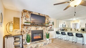 A modern kitchen with a stone fireplace, a flat-screen TV, and a ceiling fan. - Lake & Pool Access: Lazy Days Condo w/ Balcony! (Osage Beach)