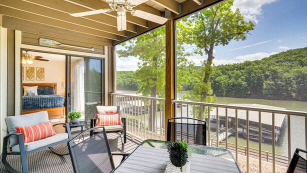 A balcony with a view of a river, a bed, and a dining table with chairs. - Lake & Pool Access: Lazy Days Condo w/ Balcony! (Osage Beach)