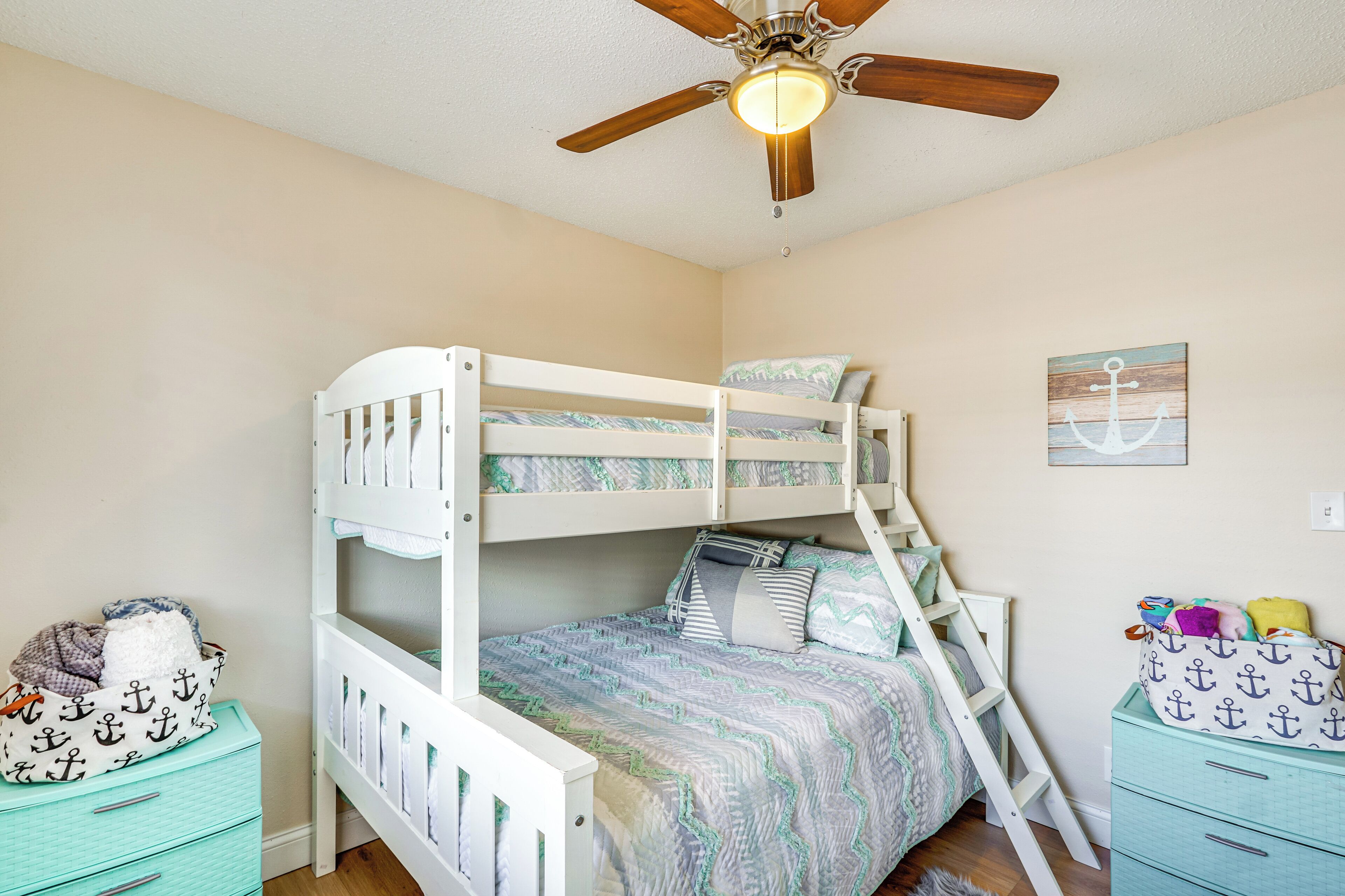 Habitación con literas, ventilador de techo, escalera y cómoda con motivos náuticos.