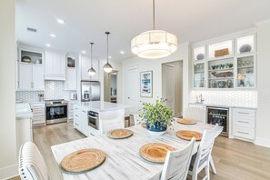 Une cuisine moderne avec des meubles blancs, un îlot central et un coin repas comprenant une table et des chaises en bois.