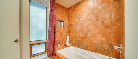 A bathroom with a bathtub, a window with a curtain, and orange tiled walls.
