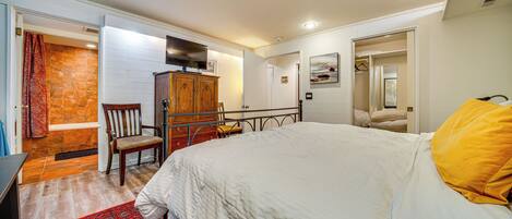 A bedroom with a large bed, a wooden wardrobe, a chair, and a television.