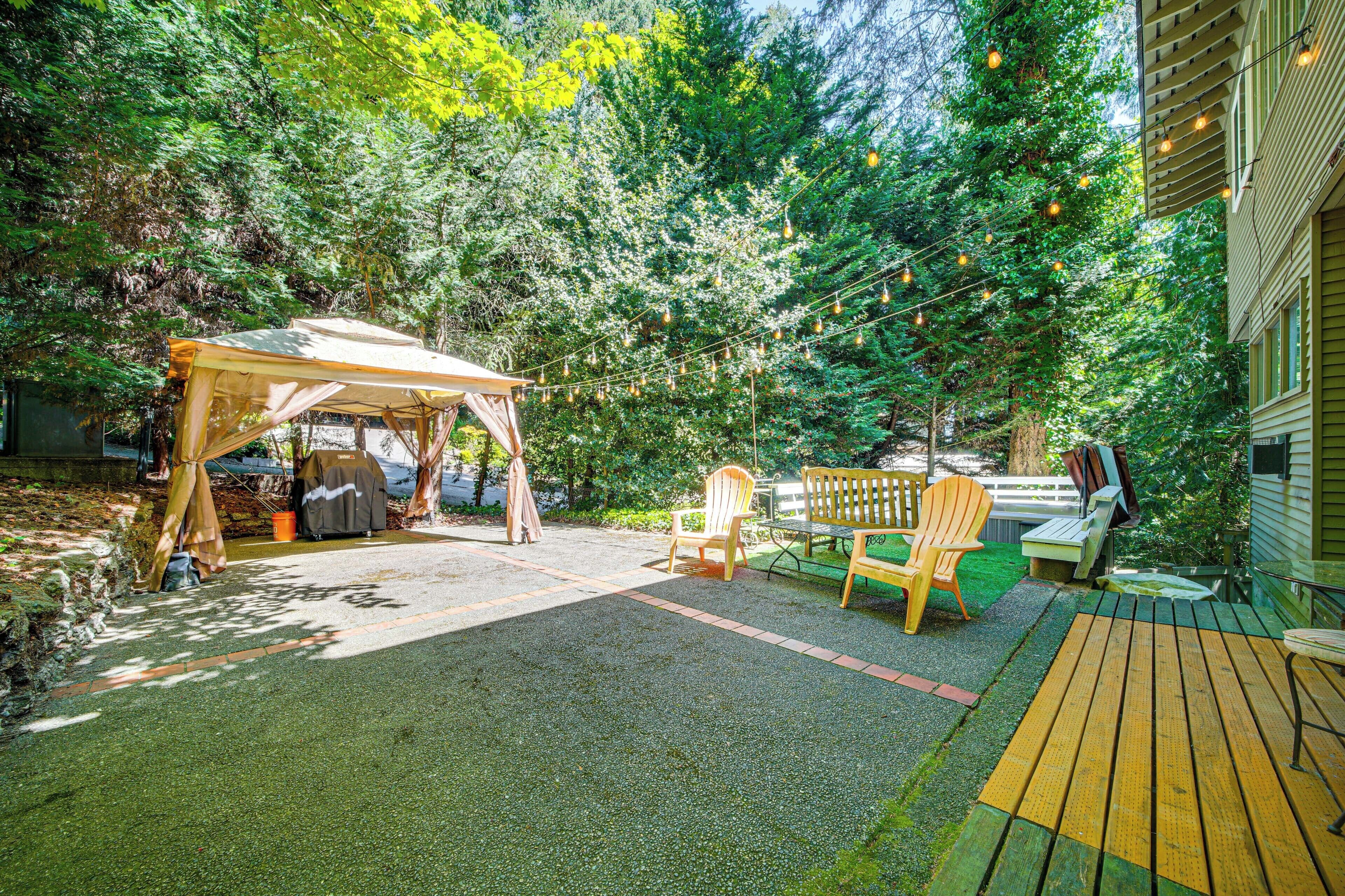 A covered outdoor seating area with a table and chairs, surrounded by trees and a wooden deck.