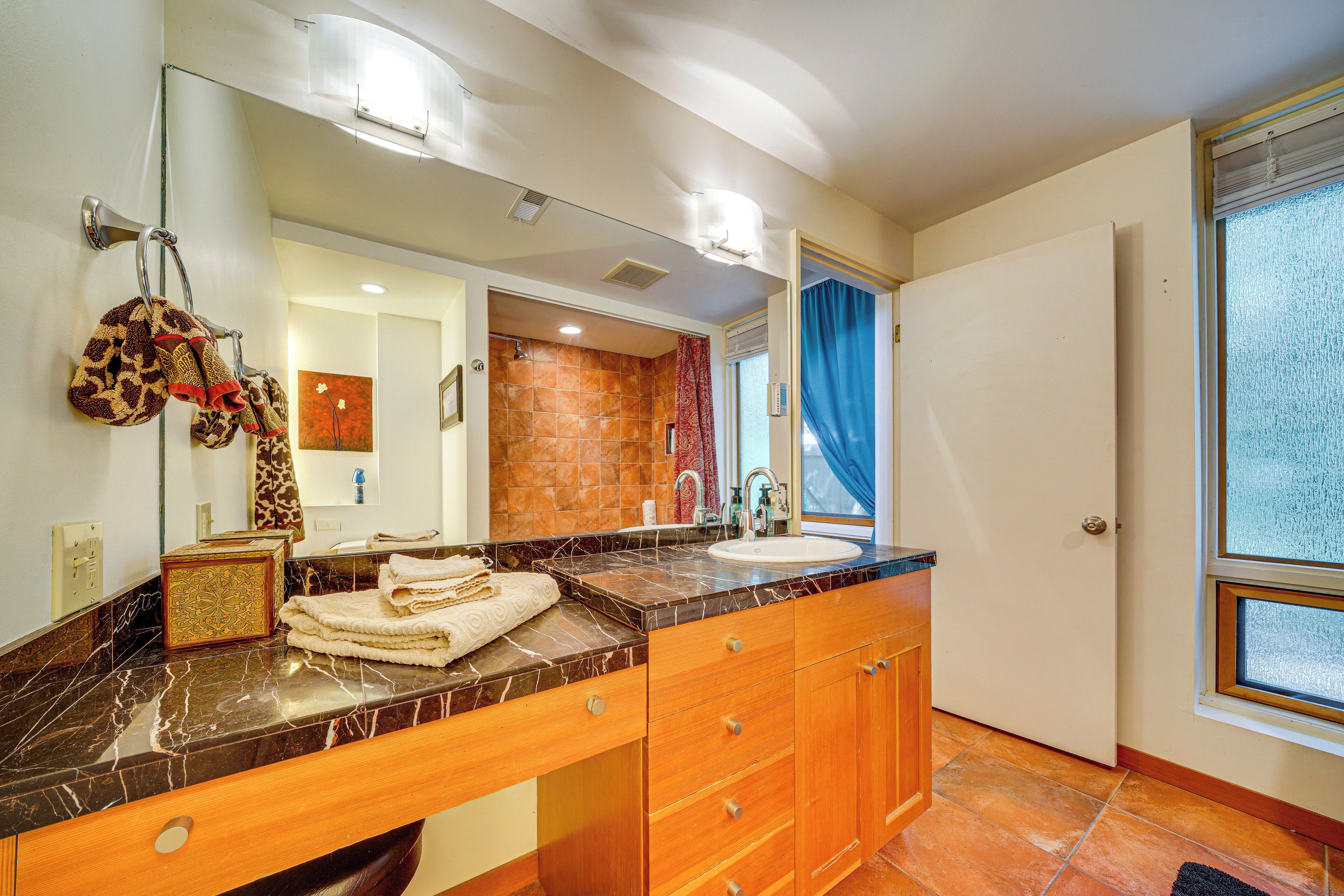 A bathroom with a marble countertop, wooden cabinets, a large mirror, and a view of the outside through a window.