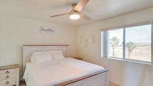 A bedroom with a bed, a nightstand, a dresser, a ceiling fan, and a window with a view of palm trees. - Pool Access & Mtn Views: Lake Havasu City Condo! (Lake Havasu City)