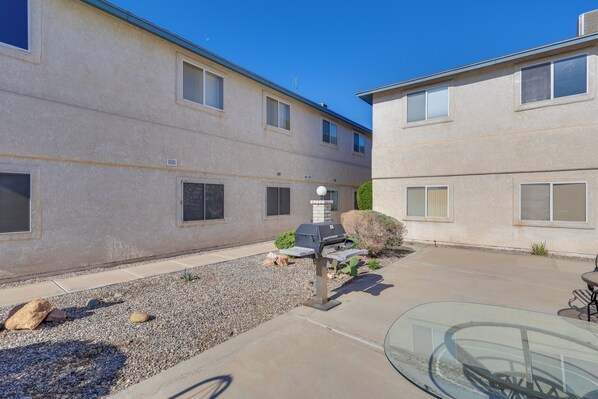 A residential building with a patio area featuring a barbecue grill, a glass table, and a small garden with rocks and plants.