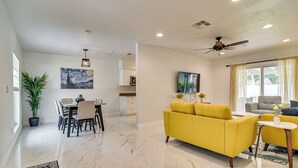 A modern living room with a yellow sofa, a dining area with a table and chairs, and a kitchen in the background.