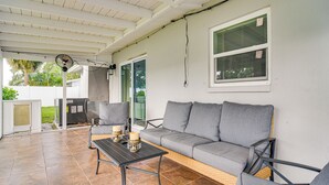 A covered patio area with a grey sofa, two armchairs, a table with candles, and a fan.
