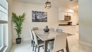 A dining area with a marble table, chairs, a potted plant, and a painting on the wall.