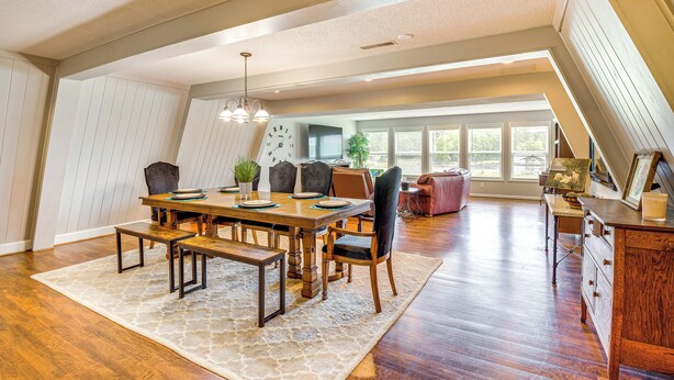 Une salle à manger spacieuse avec une table en bois, des bancs et des chaises. Une grande fenêtre laisse entrer la lumière naturelle et offre une vue sur l’extérieur.