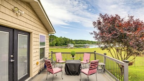 Une terrasse couverte avec une table et des chaises, une petite plante en pot et une vue sur un lac et des champs.