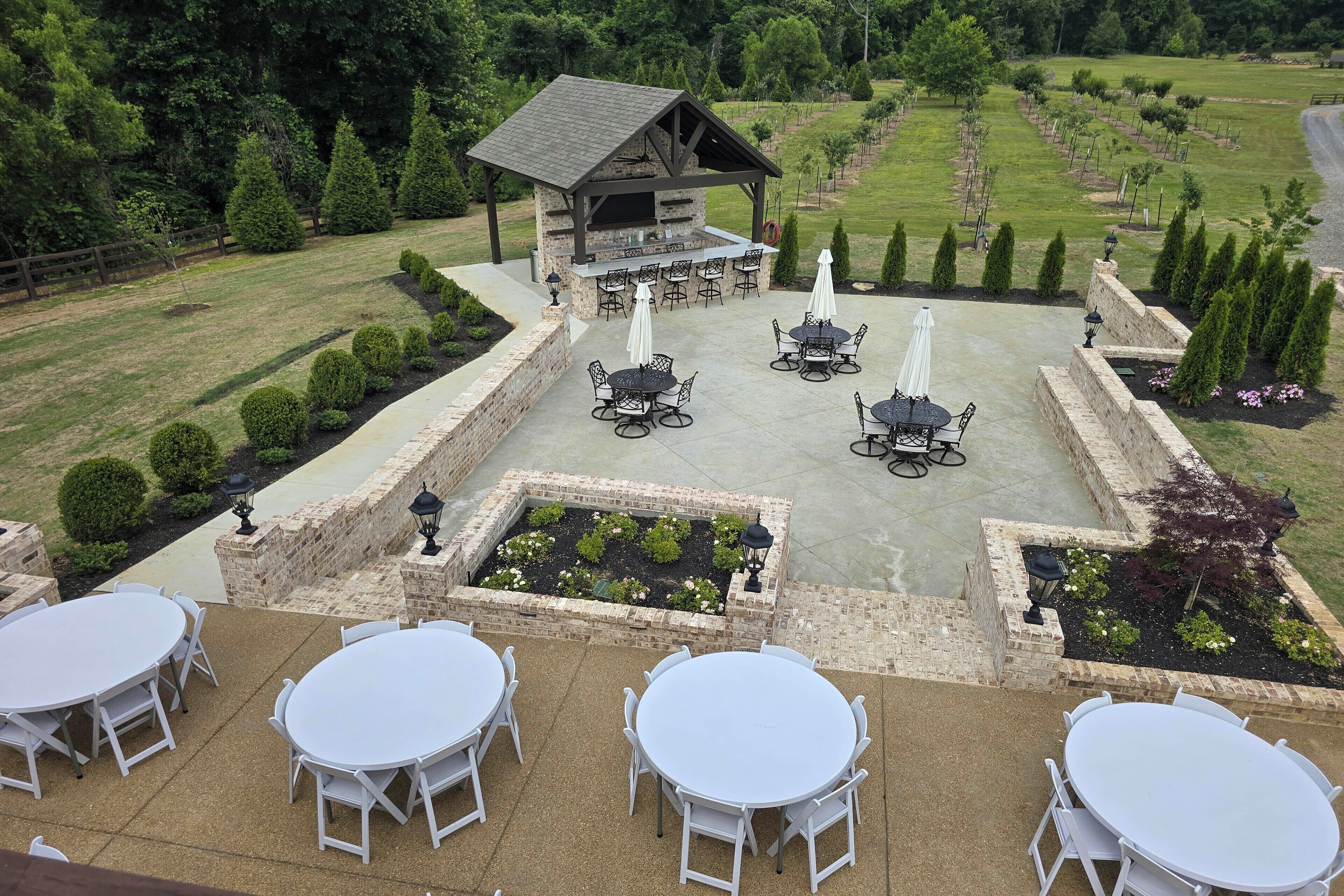 An outdoor patio area with multiple tables and chairs, a barbecue station, and a view of a landscaped garden.