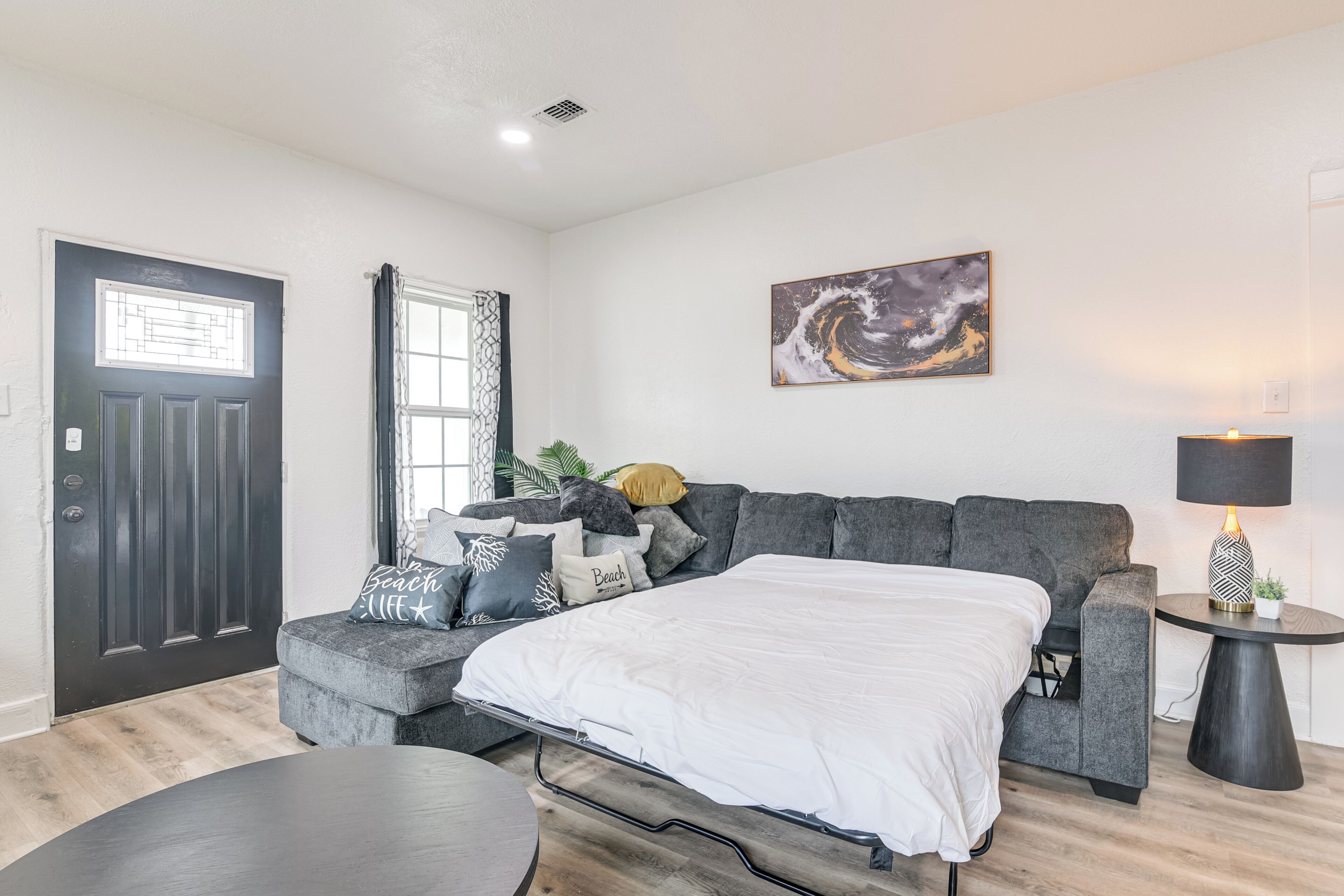 A modern bedroom with a bed, grey sofa, and a small side table with a lamp.