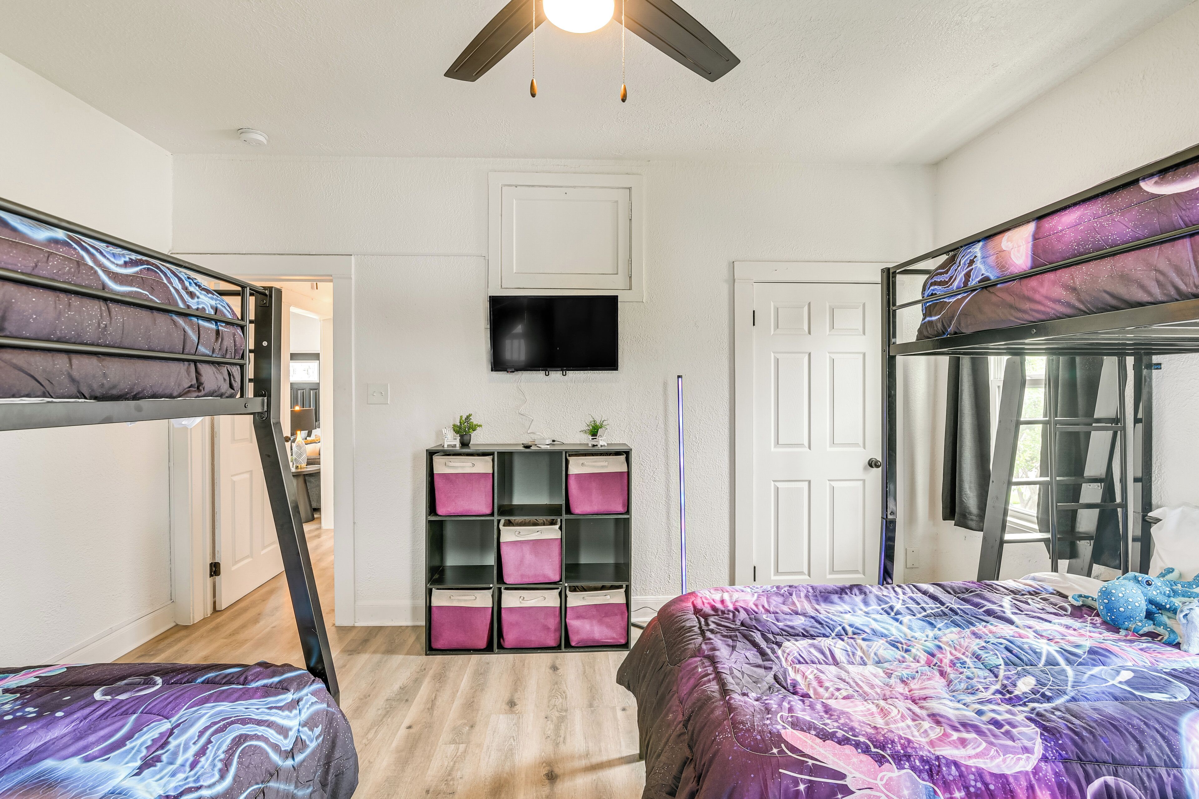 A bedroom with bunk beds, a TV mounted on the wall, and a storage unit with pink drawers.