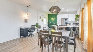A modern kitchen with white cabinets, a green accent wall, and a dining area with wooden chairs and a table. - < 1 Mi to Beaches: Galveston Retreat w/ Patio! (Galveston)