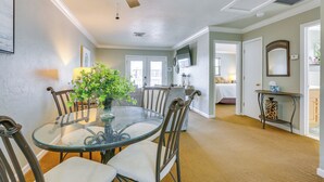 A dining area with a glass table, metal chairs, a ceiling fan, and a view into the adjacent bedroom.