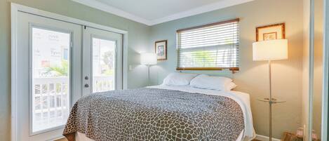 A bedroom with a bed, a door, a window with blinds, a floor lamp, and a picture on the wall.