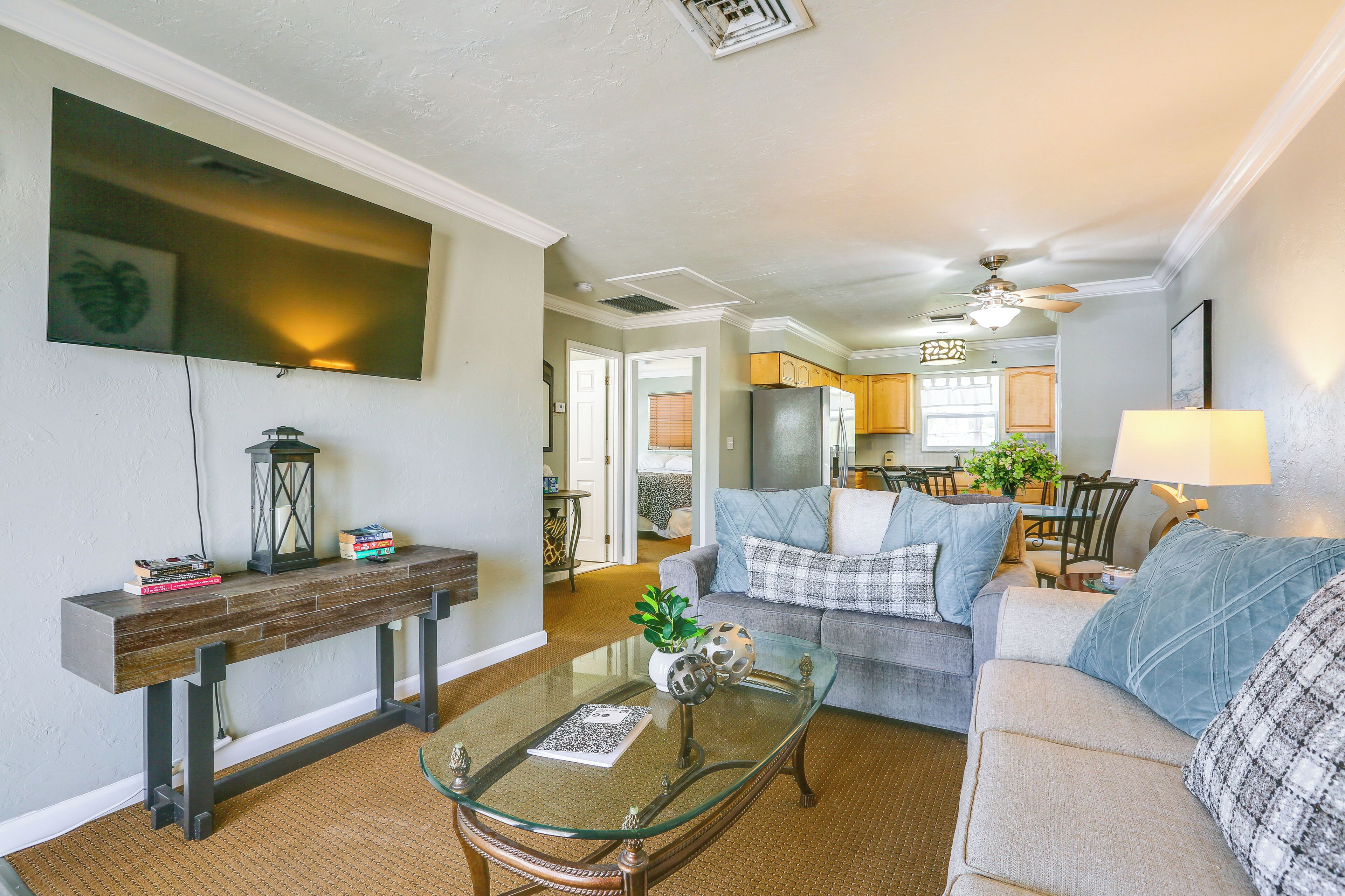 A living room with a glass coffee table, a sofa, and a TV mounted on the wall.