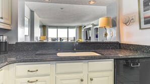 A kitchen with a granite countertop, white cabinets, a sink, and a dishwasher. - Oceanfront Resort Condo w/ Pools in Myrtle Beach (Myrtle Beach)