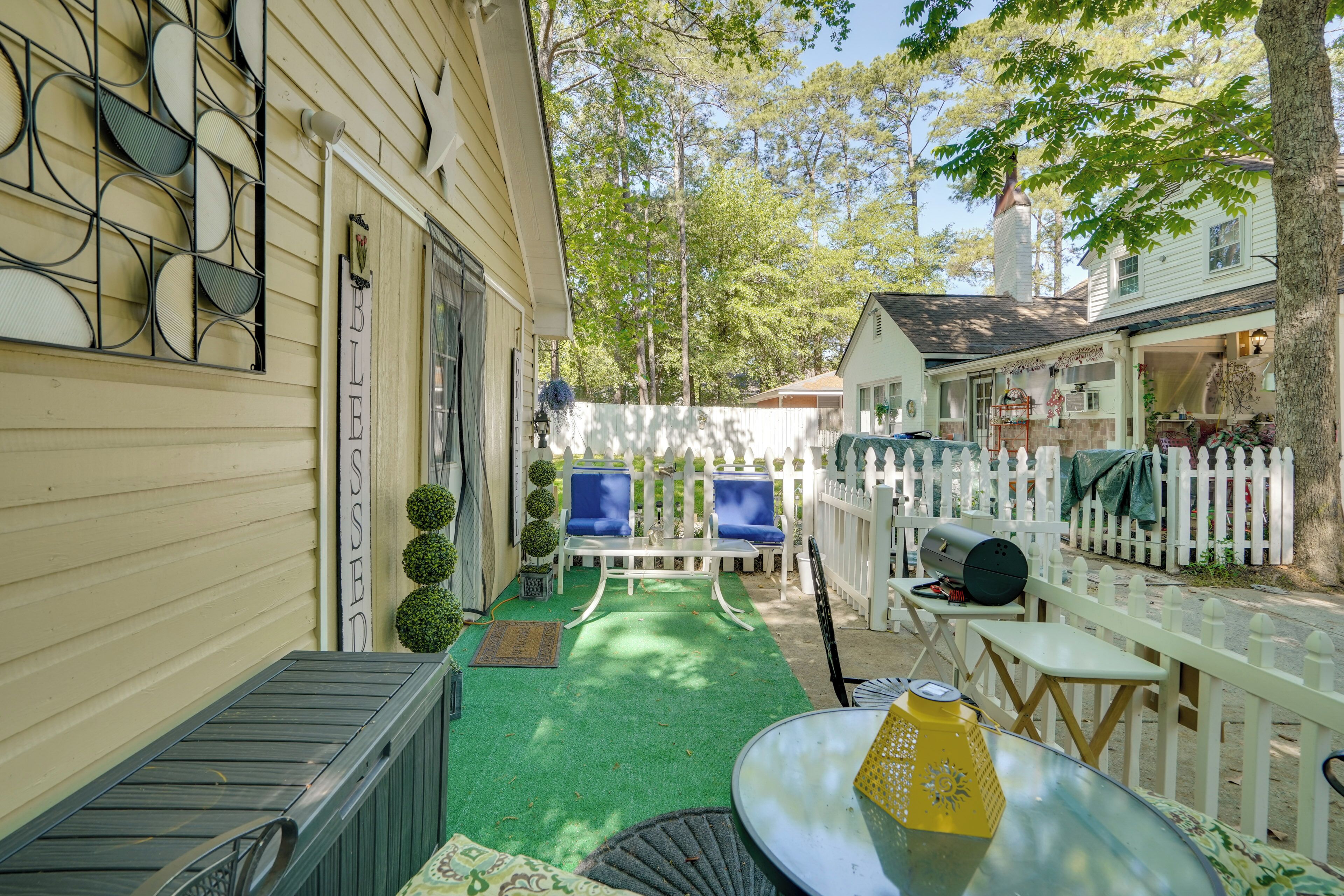 A patio with a green artificial turf, a white fence, and a white building with a chimney.