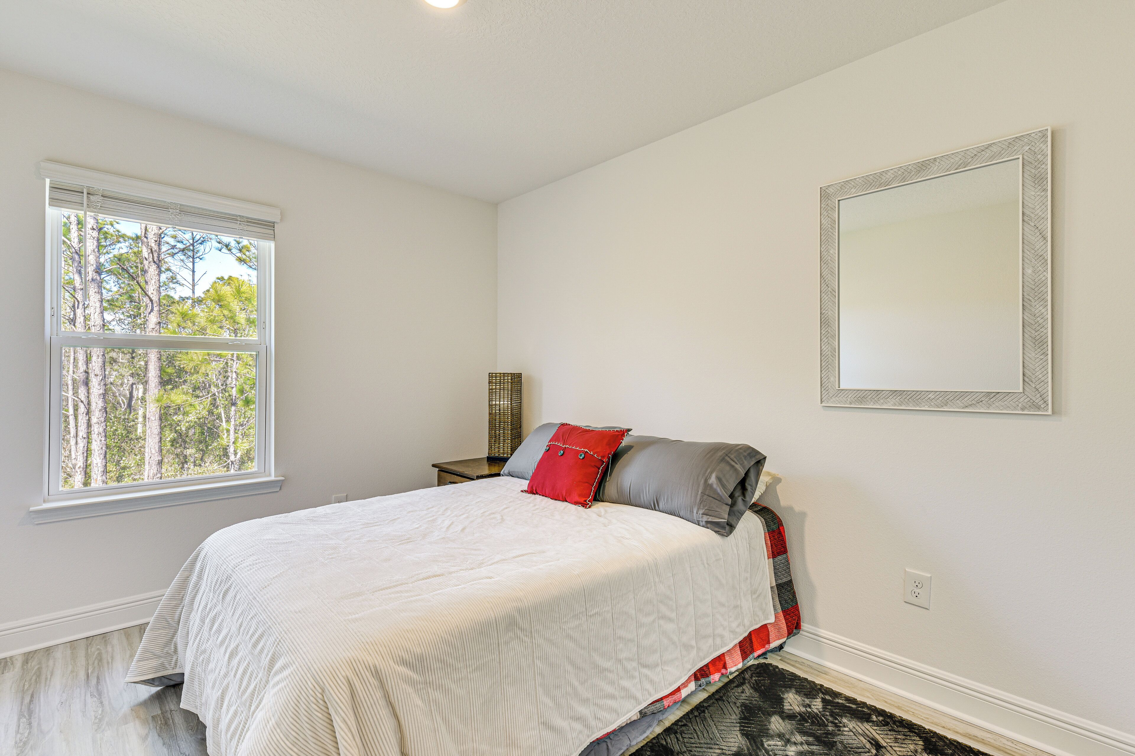 A bedroom with a bed, a window, a nightstand, and a mirror.