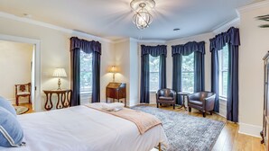 Une chambre bien éclairée, avec un grand lit, un bureau, deux chaises et un lustre.