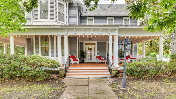 Une maison à deux étages avec un porche, des marches menant à l’entrée et un espace salon extérieur.