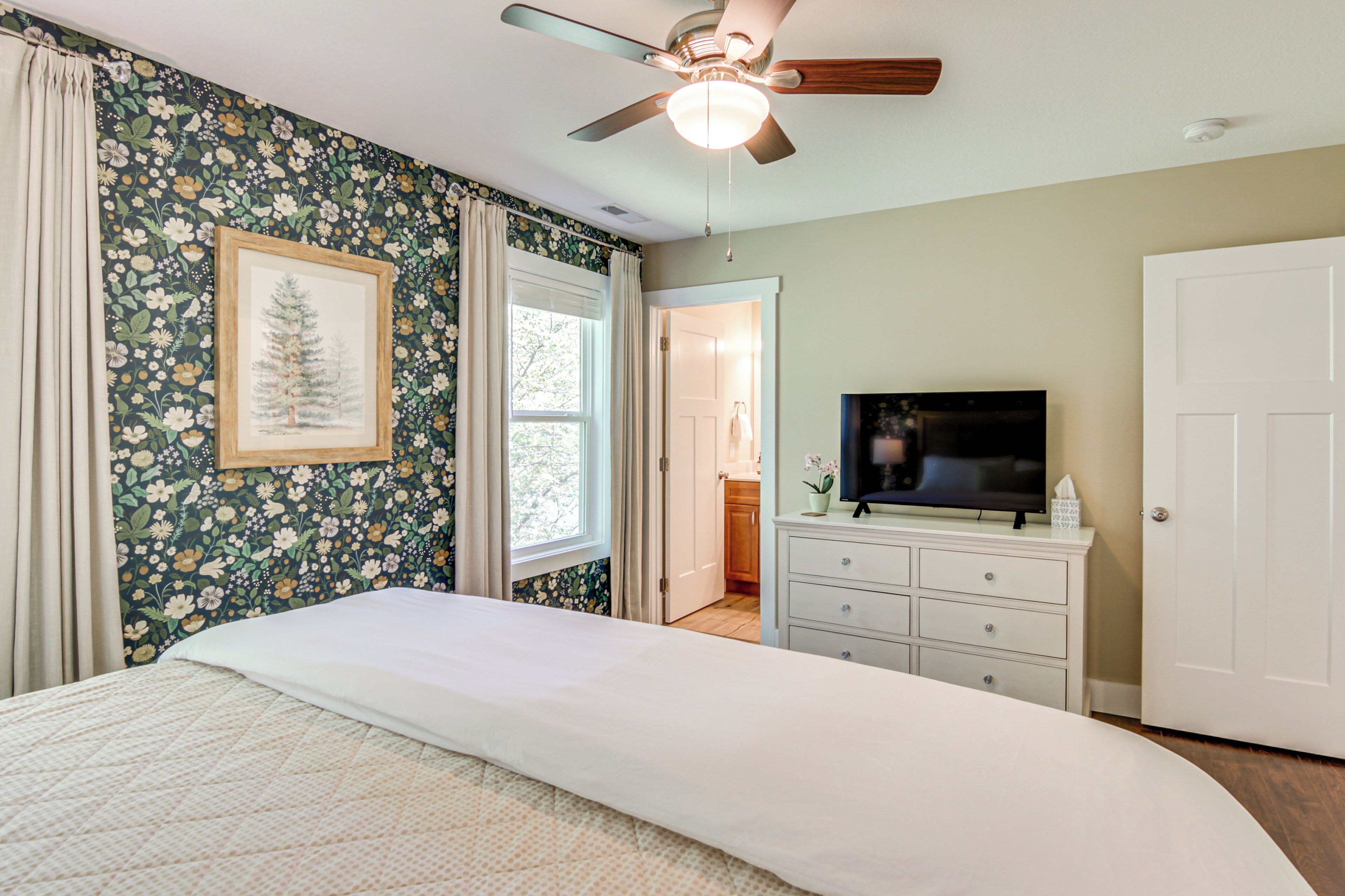 A bedroom with a bed, a ceiling fan, a TV, and a dresser.