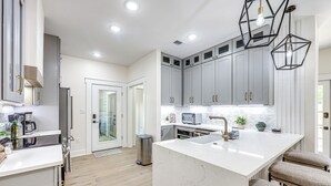 Une cuisine moderne avec des meubles gris, un îlot central blanc et des luminaires suspendus.