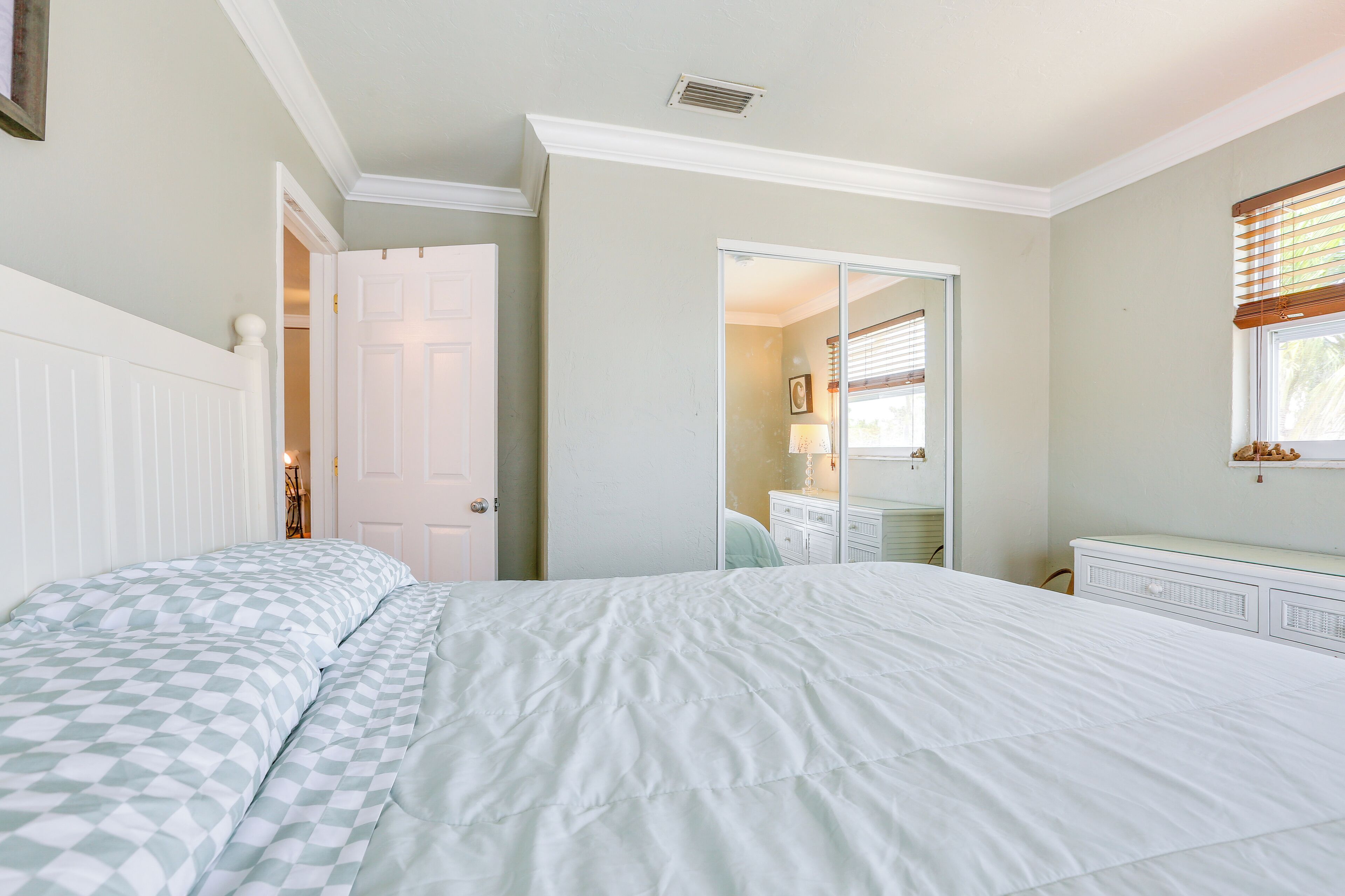 A bedroom with a large bed, a dresser, a mirror, and a door leading to another room.