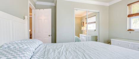 A bedroom with a large bed, a dresser, a mirror, and a door leading to another room.