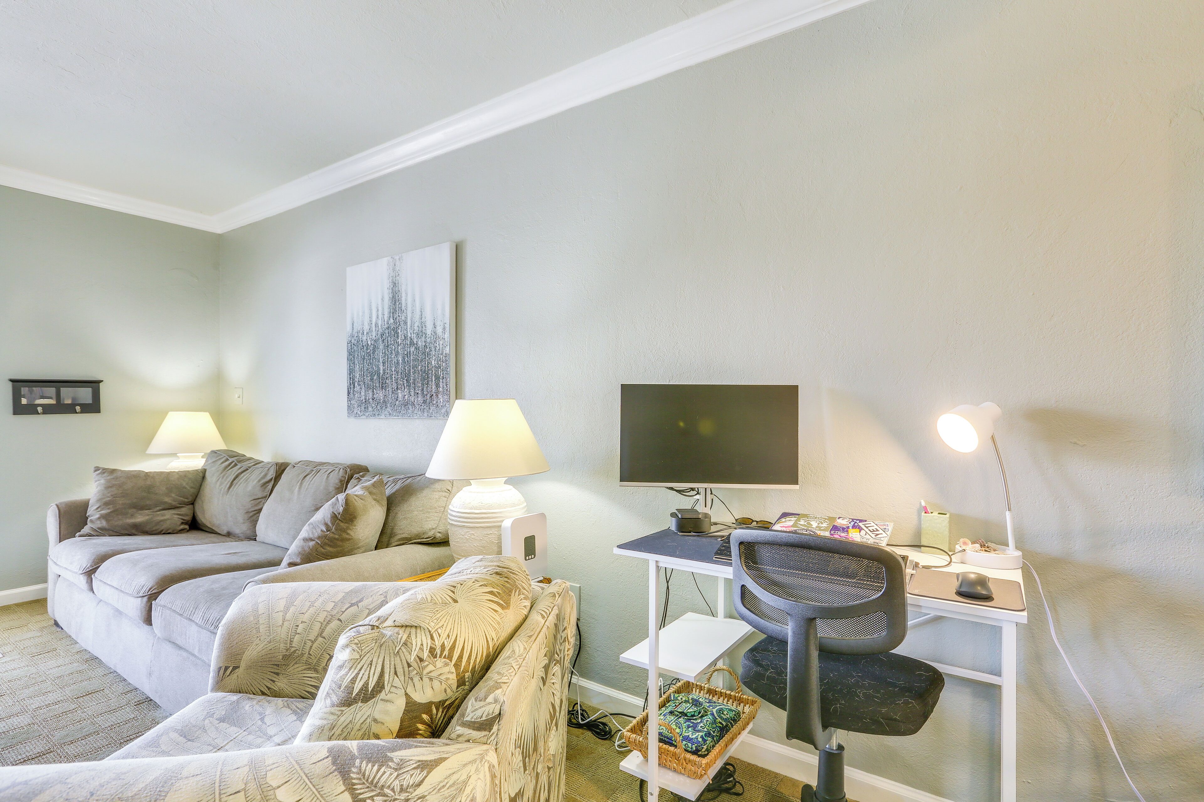 Ein Wohnzimmer mit einer Couch, einem Sessel, einem Schreibtisch mit Computer und einem Fernseher.