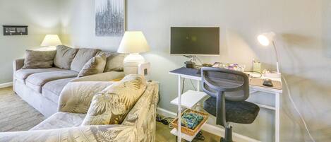 Un salon avec un canapé, un fauteuil, un bureau avec un ordinateur et un téléviseur.