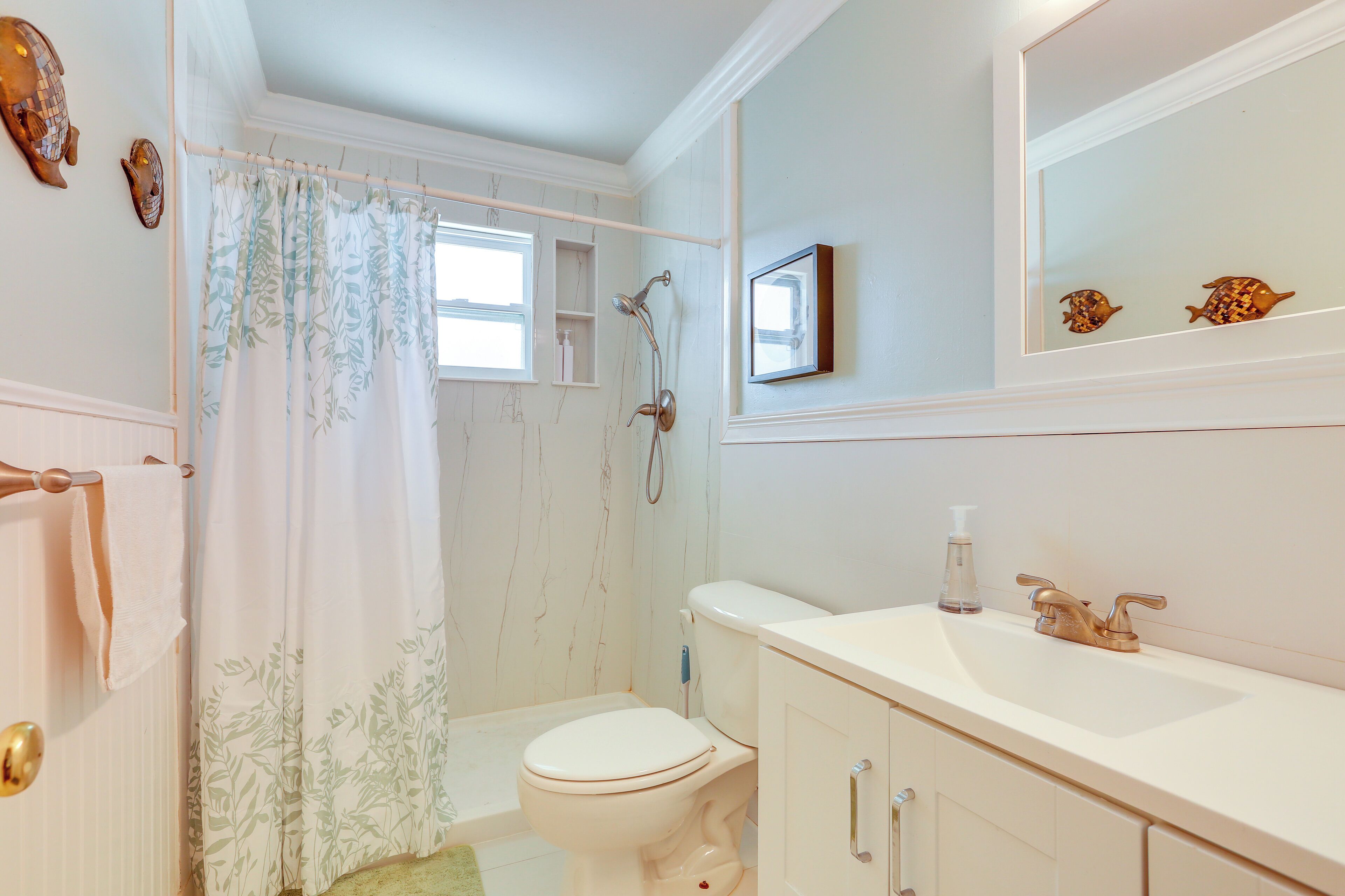 A bathroom with a toilet, shower, sink, and a mirror.