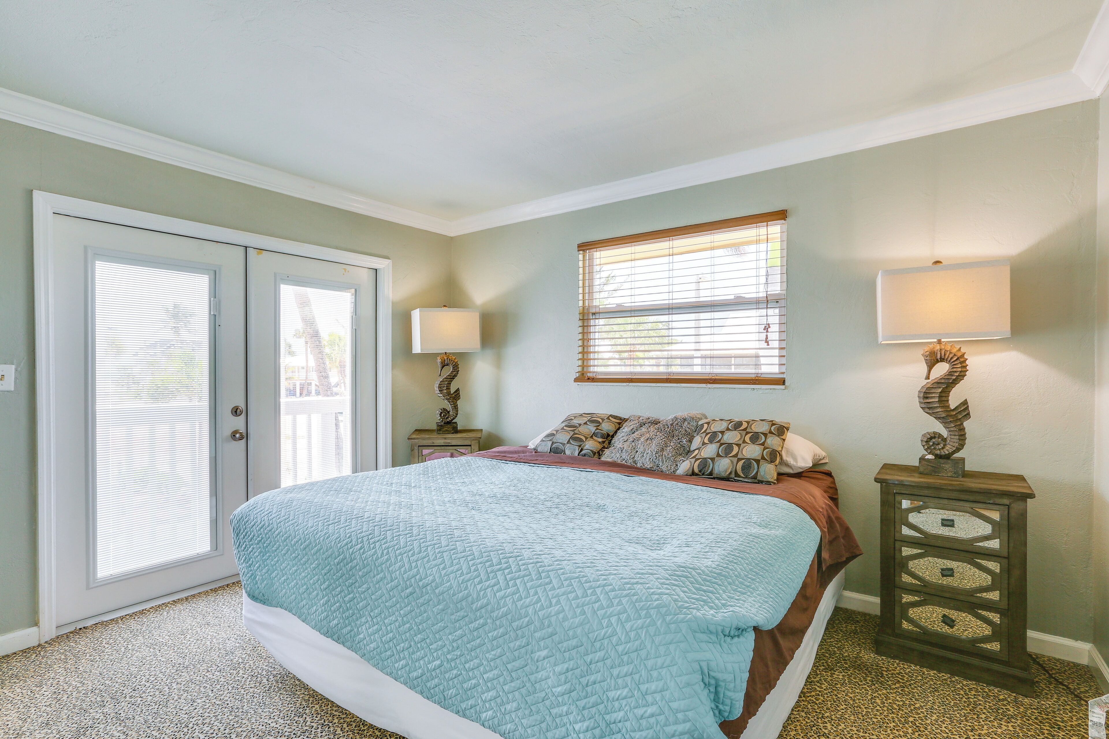 A bedroom with a bed, two bedside tables, a window with blinds, and a door.