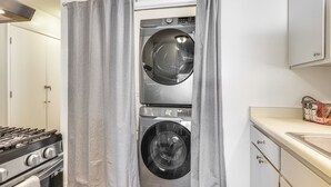 A compact laundry room with a front-loading washer and dryer, a stove, and a sink.