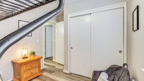 A staircase with a metal handrail, a wooden dresser with a lamp, a white door, and a black bag on the floor.